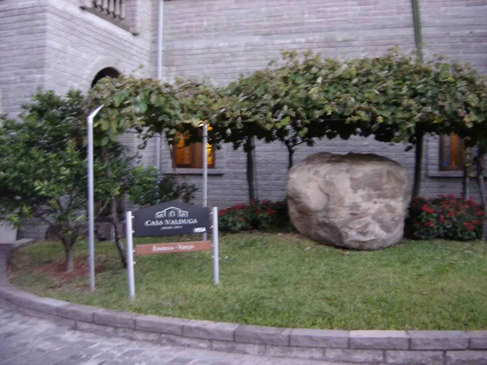 Placa da Casa Valduga no jardim, sob uma pérgola de parreira