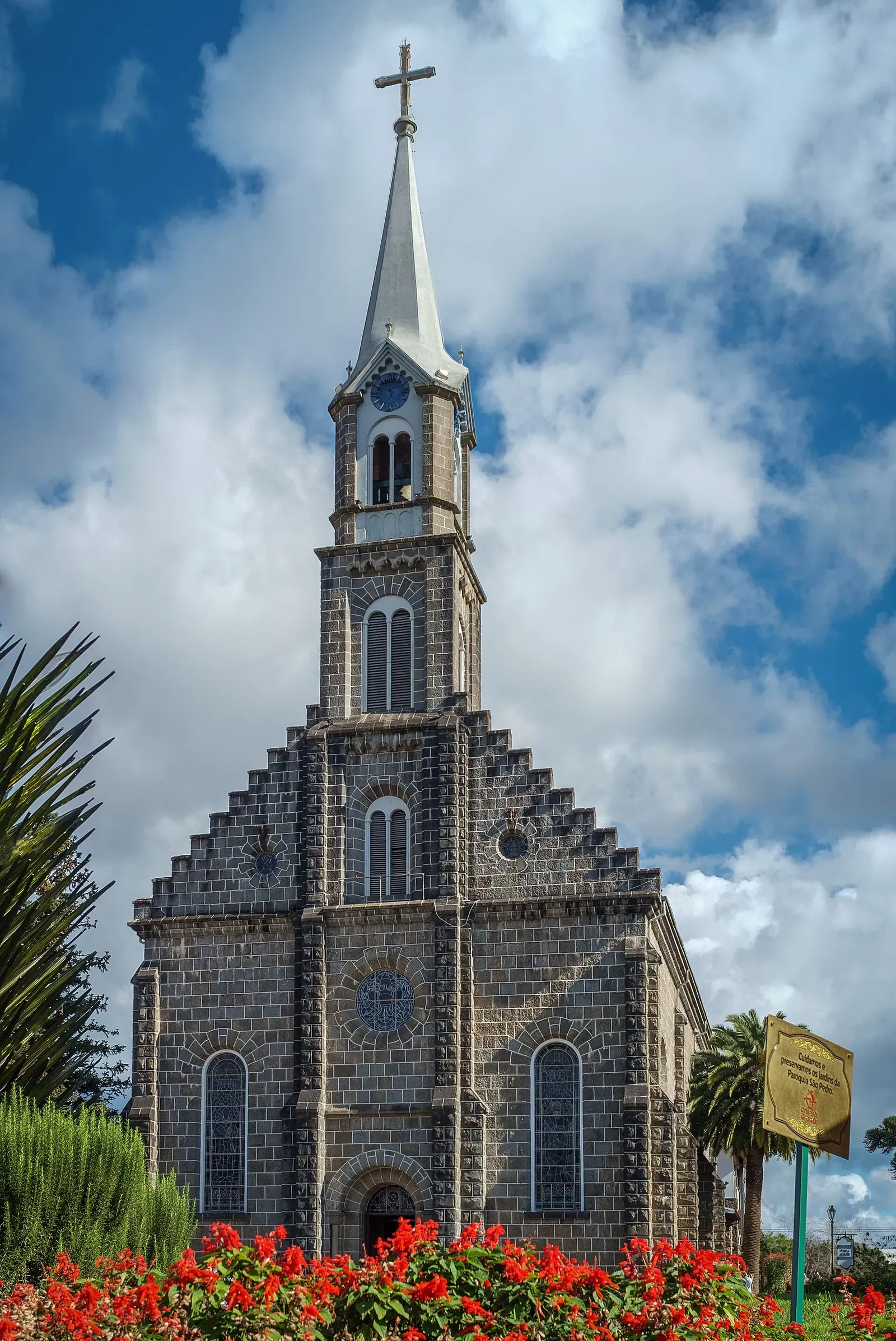 Fachada de pedra basalto da Igreja Matriz São Pedro, com a torre e flores vermelhas na frente