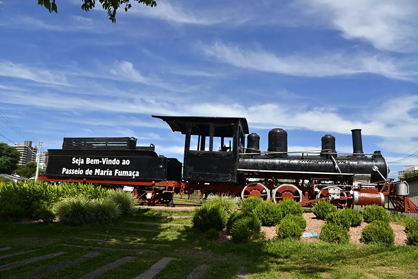 Locomotiva a vapor exposta com a placa de boas-vindas ao passeio de Maria Fumaça